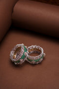 Diamond and emerald wide bangles on a tan backdrop
