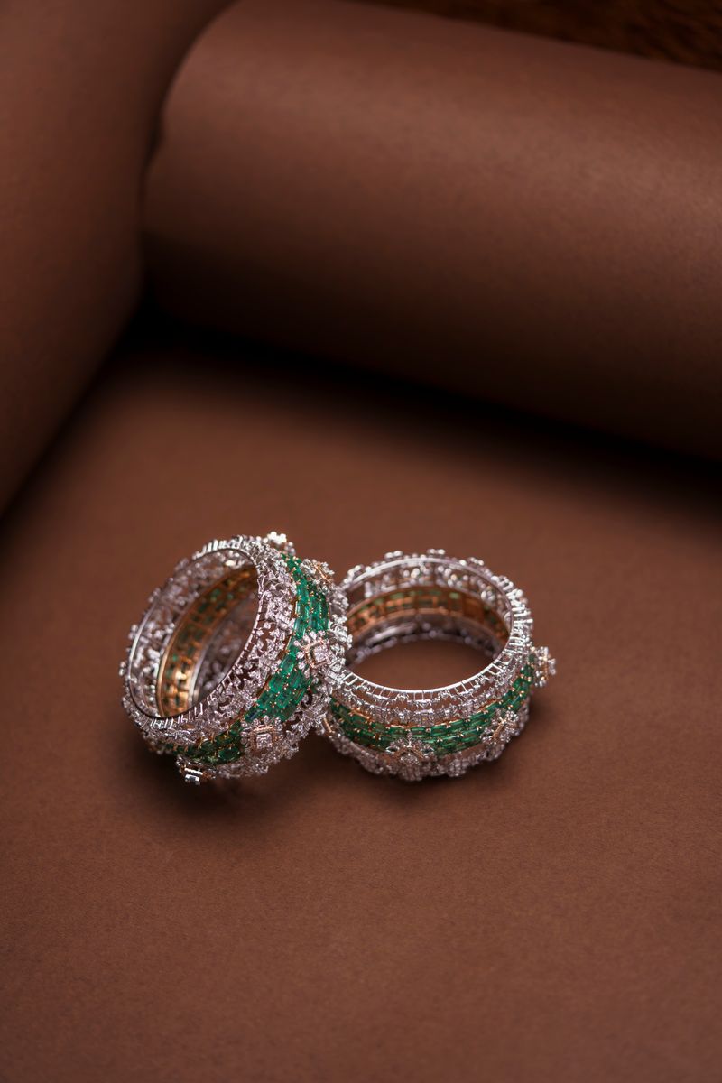 Diamond and emerald wide bangles on a tan backdrop