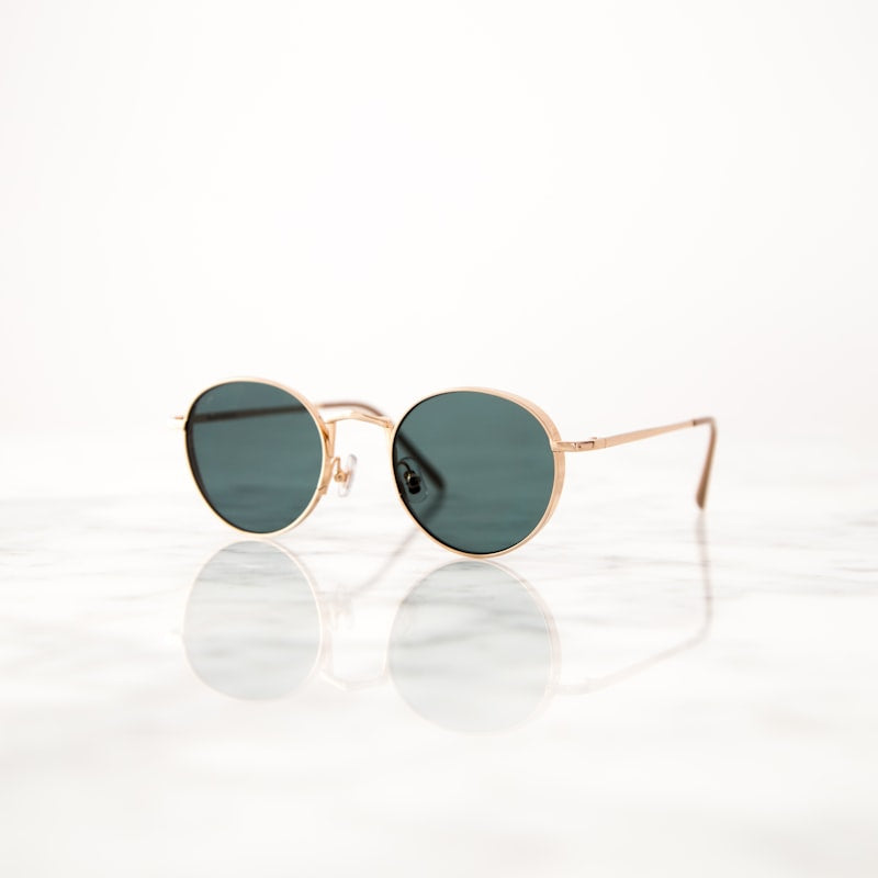 Gold round-frame sunglasses with tinted lenses on marble