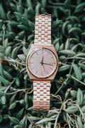 Rose-gold bracelet wristwatch resting on green foliage