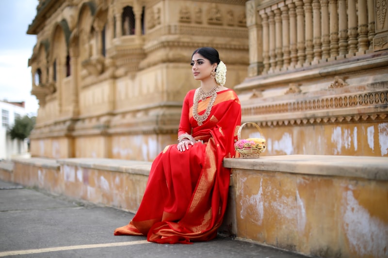 Woman in a red silk saree with gold border seated by ornate temple pillars