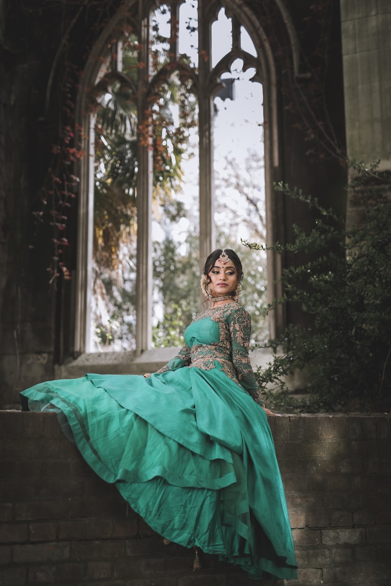 Woman in an emerald green embroidered lehenga seated by an arched window