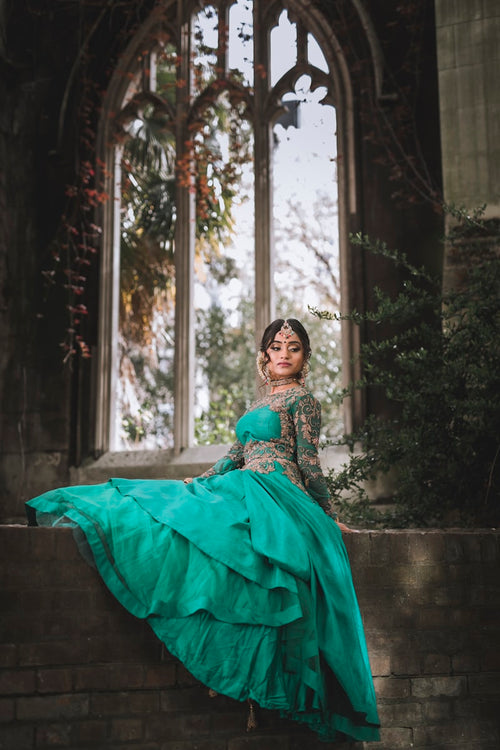 Woman in an emerald green embroidered lehenga seated by an arched window